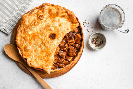 Beef steak pie with dark beer gravy and crispy puff pastry on light stone background, top view....