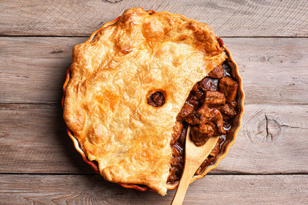 Beef steak pie with dark beer gravy and crispy puff pastry on rustic wooden background, top view.の写真素材