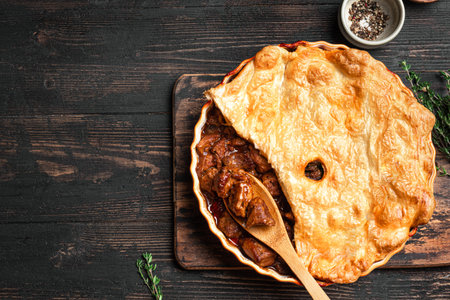 Beef steak pie with dark beer gravy and crispy puff pastry on rustic wooden background, top view. Homemade meat ale pie recipe template.の写真素材