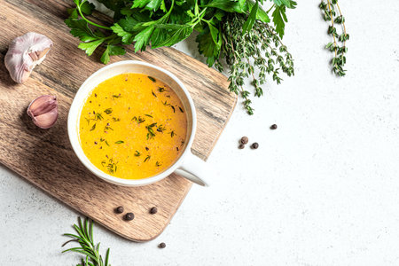 Beef bone broth with herbs (instant bouillon) in mug on white background with herbs and spices, top view, copy space. Healthy food, drinkable collagen broth.の写真素材
