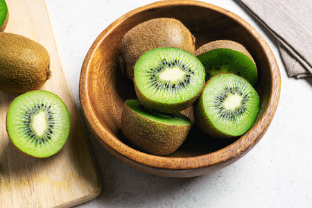 Kiwi fruits on wooden background. Whole fruit and half pieces of green kiwi in bowl. Fresh ripe juicy kiwi. Tropical fruit. Organic fruit. Healthy eating.の写真素材