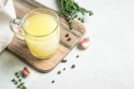 Hot healing bouillon (chicken bone broth) on white background with herbs on white background, copy space. Chicken drinkable collagen broth.の写真素材