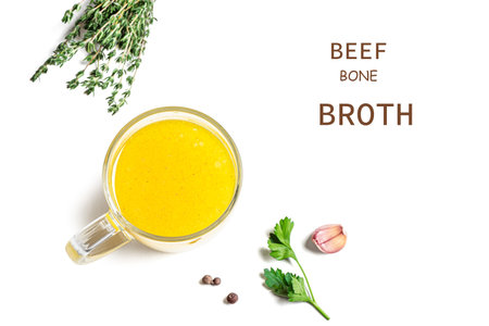 Beef bone broth, instant chicken bouillon in transparent mug isolated on white background with herbs, top view, design element. Healthy food, drinkable collagen broth.の写真素材