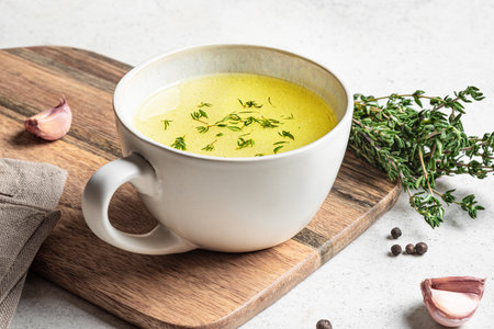 Hot healing bouillon (chicken bone broth) in mug on white background with herbs and garlic. Chicken drinkable collagen broth.の写真素材