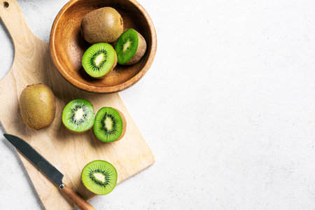 Kiwi fruits in wooden bowl. Whole fruit and half pieces of green kiwi on white table, top view, copy space. Fresh ripe kiwi. Organic healthy eating.の写真素材