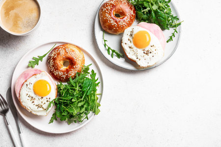 Bagel sandwich with fried egg, cheese, ham and greens, white background, top view, copy space. Healthy balanced breakfast for two, breakfast together, healthy eating concept.の写真素材
