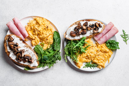 Healthy balanced breakfast plates. Scrambled eggs, greens, ham, sandwich with cream cheese and fried mushrooms. Breakfast for two, top view.の写真素材
