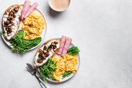 Healthy balanced breakfast plates. Scrambled eggs, greens, ham, sandwich with cream cheese and fried...