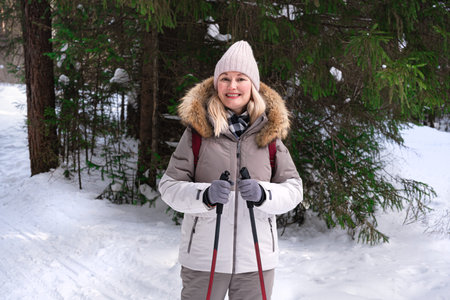 Woman practicing nordic walking with nordic walking poles. Happy middle aged woman hiking in winter park or snow forest, healthy winter activity.の写真素材
