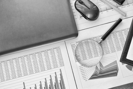 Financial printed paper charts, graphs, diagrams, computer, pen, and calculator on wooden desk.の写真素材