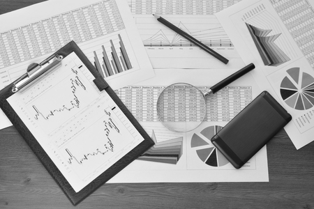 Financial printed paper charts, graphs, diagrams, computer, pen, and calculator on wooden desk.の写真素材