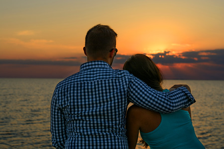 Two lovers (pair) in an embrace sit on the seashore and look at the sunset. Romance and Travelの写真素材