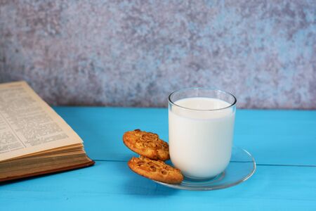 A glass of milk, homemade cakes (oatmeal cookies with nuts) and a book on a blue wooden background.の写真素材