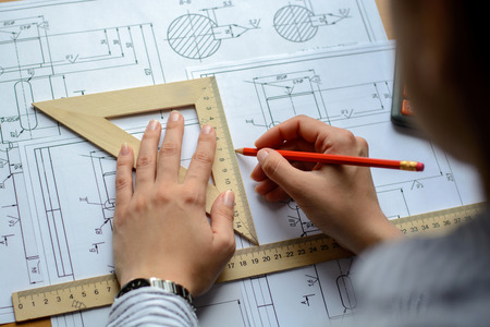 Girl architect draws a plan, graph, design, geometric shapes by pencil on large sheet of paper at...