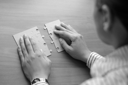 Female hands on a wooden office desk pick puzzleの写真素材