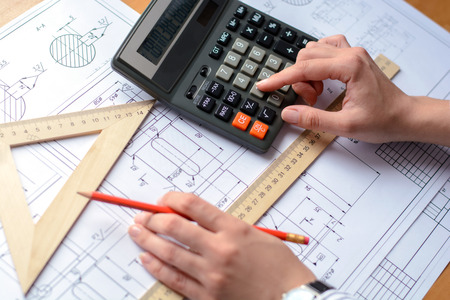 Girl architect draws a plan, graph, design, geometric shapes by pencil on large sheet of paper at office desk. Soft focusの写真素材