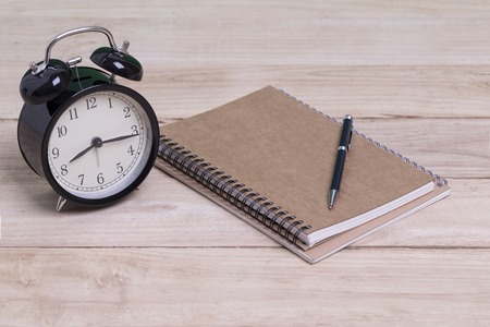 Old retro alarm clock and book with pen on tableの写真素材