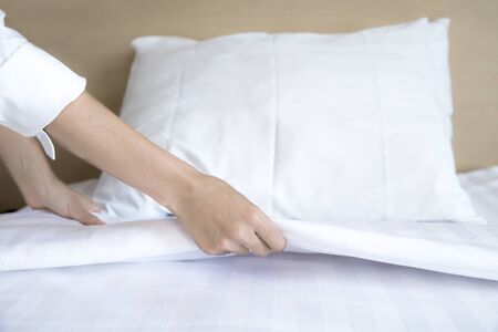 Close up hand set up white bed sheet in hotel roomの写真素材