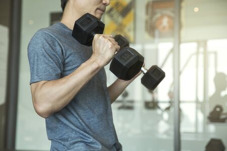 Young man beginner exercising with dumbbell flexing muscles at gym, sport training conceptの写真素材