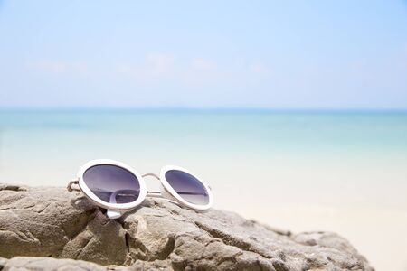 Sunglasses on tropical beach rock of blue sea in summerの写真素材