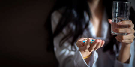 Close up Asian woman holding pill capsule and a glass of water in young female handの写真素材