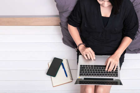 Top view of a young asian woman using laptop computer sitting on wooden floor at home , work from...