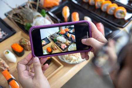 Woman photographing food served Japanese sushi set , Sushi nigiri rolls and sashimi in japanese food...