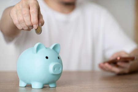 Close up businessman hand putting money coin into piggy for saving money, budget, investment or...