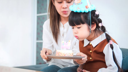 Party with mother for little girl birthday in living room, Asia children girl blows out birthday...