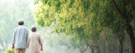Elderly couple walking together in peaceful green park with trees and soft natural light creating calm atmosphereの素材