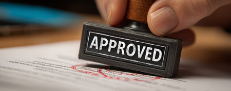 Approved stamp on contract document with hand pressing seal conveying official authorization and positive emotionの素材