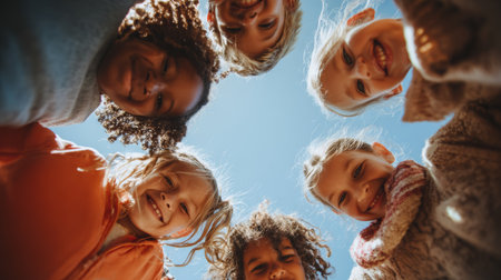 Group of diverse children smiling happily in circle outdoors under clear blue sky on sunny dayの素材