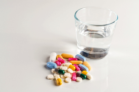 Assorted pills, capsules with a glass of water on white background.の写真素材