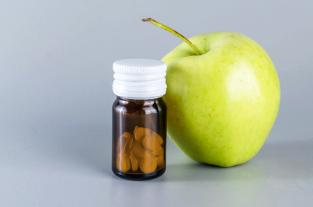 A glass medicine with a green apple on a gray background.の写真素材