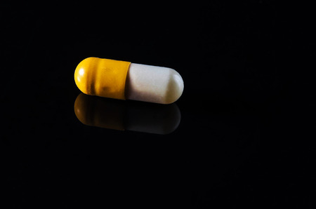 Single yellow-white capsule on reflective black background.の写真素材