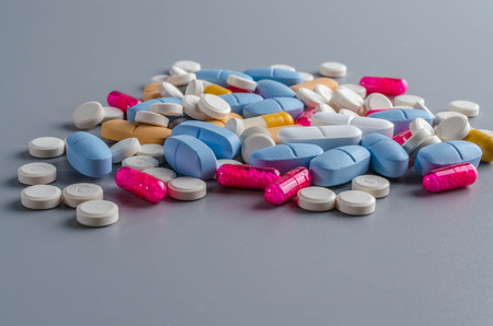 Assorted pharmaceutical medicines pill, tablets and capsules on gray background.