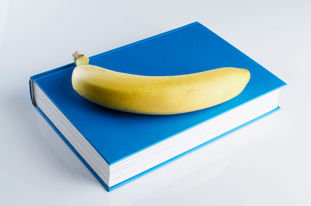 Blue book with a banana on a white background.の写真素材