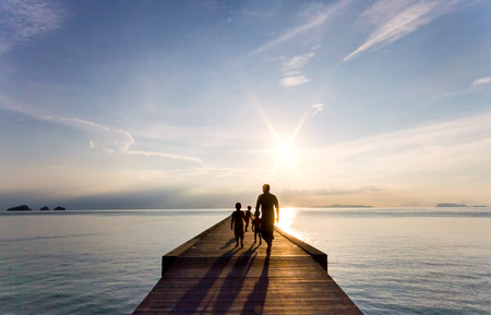Father and children are walking along the pier at sunsetの写真素材
