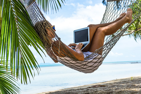 Young woman working on the laptop in a hammock on a tropical beacの写真素材