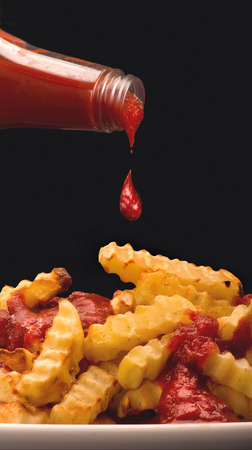Pouring ketchup over golden wedge french fries.