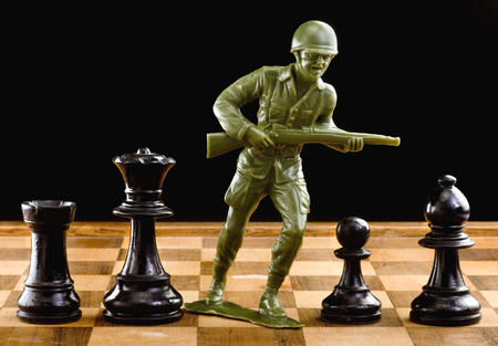 Chessmen with green toy soldier taking on to battle.