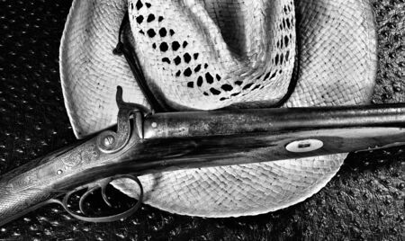 Antique shotgun and old straw cowboy hat in black and white.
