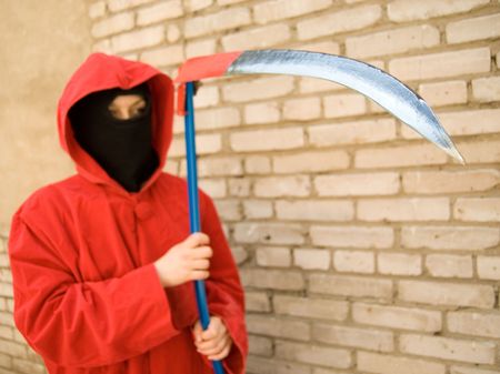 Spooky figure in red hood holding a sharp scythe. Focus is on a scythe but person is out of fucusの写真素材