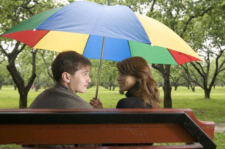Happy young couple on a bench under a colorful umbrellaの写真素材