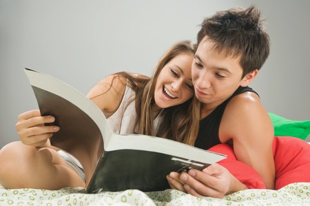 Happy young couple in bed reading a magazine togetherの写真素材