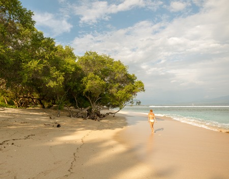 Young woman walking along tropical beach at Gili islands, Indonesiaの写真素材