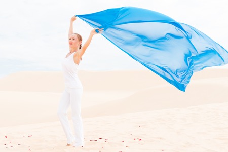 Young slim woman wearing white with flying blue scarf in desertの写真素材