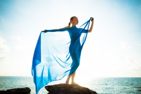 Freedom and beauty concept. Beautiful girl with blue scarf standing on the Rock. Flying. Free. Vacationの写真素材