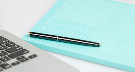 closed pen on an closed blue notebook and laptop in a background. studio shot on white background