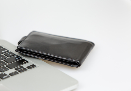 black leather wallet lying beside a laptop on a desk. studio shot on a white background. closeup
